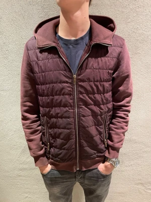 Reiss cardigan  - Säljer en mörkröd pufferjacka med quiltad framsida och mjuka ärmar. Jackan har huva, dragkedja framtill och två fickor med dragkedja. Perfekt för dig som vill ha en casual och snygg look till höst och vinter. 