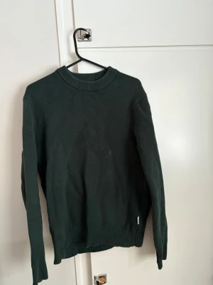 Tjockare stickad tröja - En enkel och stilren mörkgrön stickad tröja med rund halsringning och ribbade muddar vid ärmslut och nederkant. Perfekt för lager på lager under kyliga dagar och passar till både jeans och kjol. 