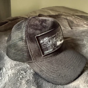 Svart meshkeps från OneCap - Säljer en svart keps från OneCap med mesh på sidorna och baksidan. Framsidan har en stor patch med svartvitt stadslandskap. Kepsen har böjd skärm och justerbar passform. Perfekt för dig som gillar streetwear och vill ha en unik accessoar.