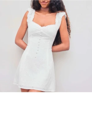 Vit kort klänning med broderade blommor - Superfin vit kortklänning med broderade blommor och dekorativa knappar framtill. 