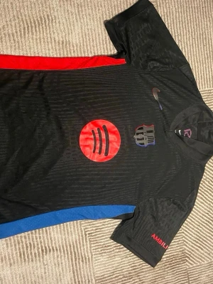 Nike FC Barcelona svart matchtröja M - Säljer en svart FC Barcelona matchtröja från Nike med röda och blå detaljer på sidorna. Tröjan har tryckta loggor, Spotify sponsor på bröstet och Dri-FIT ADV-teknologi för extra komfort. Perfekt för dig som älskar fotboll och vill ha en unik Barca-tröja.