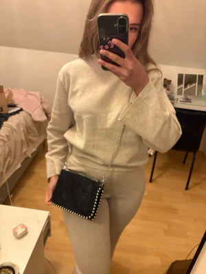 Svart axelväska med silverdetaljer - Snygg svart axelväska i mocka med silverfärgad kedja och coola nitar längs kanterna. Väskan har dragkedja upptill och flera fack inuti för att hålla ordning på dina grejer. Perfekt storlek för det viktigaste och passar till många outfits. Felfri , nypris 260kr!