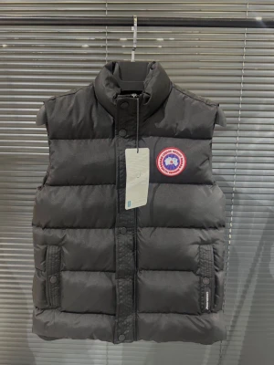 Svart dunväst från Canada Goose - Säljer en svart dunväst från Canada Goose med hög krage och klassisk logotyp på bröstet. Västen har tryckknappar och dragkedja framtill samt två fickor med knappstängning.  Storlek S-XL finns
