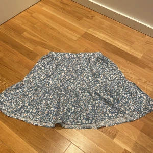 Blommig blå kortkjol från SHEIN - Supersöt blå kortkjol från SHEIN med vitt och orange blommönster. Kjolen har resår i midjan och ett flowy fall som ger en avslappnad vibe. Perfekt för dig som gillar en feminin och trendig stil. Passar dig som vill ha något lätt och luftigt.