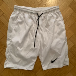 Vita Nike shorts - Säljer ett par vita Nike shorts med svart snörning i midjan och klassisk Nike-logga på ena benet.