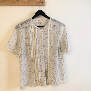 Söt vintage blus med spetsdetalj - Säljer en söt vit-blå prickig kortärmad blus från  Smiley Vintage. Tunnt luftigt material. Perfekt för alldagligt men elegant mode. Storlek S.