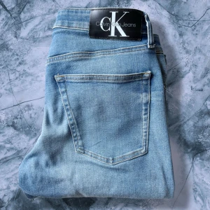 Calvin Klein ljusblå slim jeans - Snygga ljusblå jeans från Calvin Klein med klassisk femficksdesign och diskret CK-logga på bakfickan. Jeansen har slim passform, normal midja och är tillverkade i mjukt denimtyg. Perfekta för dig som gillar en stilren och modern look.