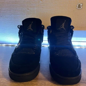 Svarta Nike Air Jordan 4 sneakers - Säljer ett par svarta Nike Air Jordan 4 sneakers med klassisk Jumpman-logga på plösen och hälen. Skorna har meshpaneler, snörning och detaljer i mocka samt plastdetaljer vid snörningen. Snygg och tidlös modell som passar till streetwear. 