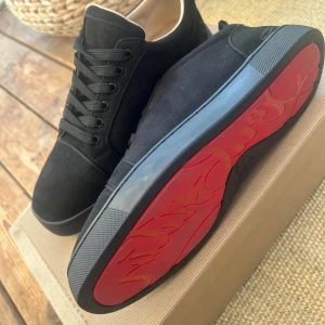 Christian Louboutin skor - Svarta sneakers från Christian Louboutin i mocka med klassisk röd sula och diskret broderad logga på hälen. Skorna har rund tå, svarta snören och platt sula. Snygg och stilren design som sticker ut med den ikoniska röda undersidan. Skorna är endast använda en gång.