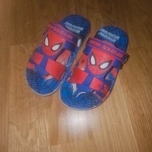 Spiderman sandaler blå/röd barn - Coola sandaler med Spiderman-motiv i blått och rött. Skorna har justerbara remmar och tydliga spindelnätsdetaljer. Perfekta för sommaren och för alla små superhjältefans som vill sticka ut på lekplatsen.