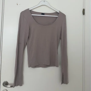 Beige långärmad topp med slits - Säljer en stilren beige långärmad topp från Gina med rundad, djup halsringning och slits vid ärmslut. Toppen är i mjuk bomull och har en slim passform som sitter snyggt på kroppen. Liten i storleken.