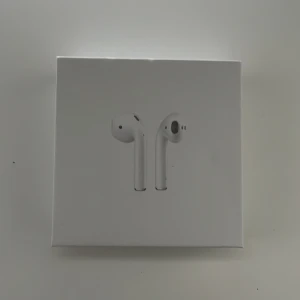 AirPods 2 - Apple AirPods 2 i originalförpackning. Trådlösa hörlurar med laddningsetui, kompatibla med iPhone och andra Apple-enheter. Produkten ser ut att vara i mycket gott skick utan synligt slitage eller repor. Perfekt för musik, samtal och smidig anslutning.