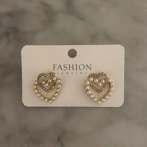 Hjärtformade örhängen i silverfärg och pärlor  - Hjärtformade örhängen i silverfärg med stenar och pärlor. 