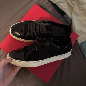 Lanvins - Snygga svarta sneakers från Lanvin med coola lackade detaljer på tån och längs kanten. Skorna har vita sulor och svarta snören, vilket ger en stilren kontrast. Perfekta för dig som gillar en clean men ändå lyxig vibe.