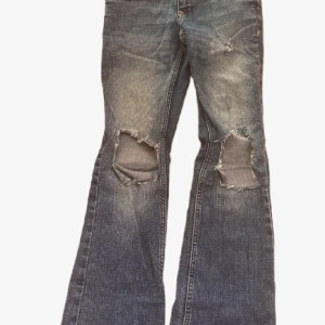 Levis bootcut jeans med slitna knän - Blå  jeans med bootcut passform och slitna, trasiga knän för en edgy look. Klassisk femficksmodell med dubbla knappar i midjan och tydliga slitningar framtill. Jeansen har en något ljusare tvätt och breda benslut.