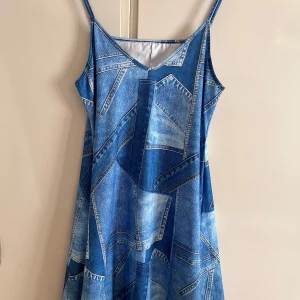 Blå klänning med jeansmönster - Säljer en blå ärmlös klänning med smala axelband och coolt jeansmönster. Klänningen har v-ringning och är i en lätt, flowy modell som ger en avslappnad vibe. Perfekt för dig som gillar unika plagg med streetkänsla.