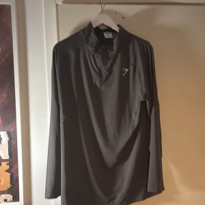 Grå Gymshark half zip träningströja Xl - Säljer en grå långärmad träningströja från Gymshark i storlek Xl. Tröjan har en smidig half zip-dragkedja framtill och är tillverkad i ett lätt och stretchigt syntetmaterial. Perfekt för gymmet eller löprundan.