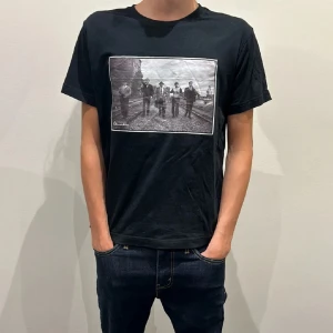 Svart celemon ace t shirt me tryck - Svart t-shirt från CelemonAce i storlek S med ett stort svartvitt print på bröstet som föreställer fem personer på järnvägsspår. Klassisk rund hals och korta ärmar. Skön och mjuk känsla, perfekt till jeans eller shorts.