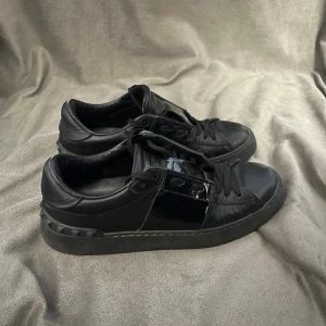 Svarta Valentino Garavani sneakers - Säljer ett par svarta Valentino Garavani sneakers med snörning och rund tå. Skorna har en platt sula och är tillverkade i skinn. Klassisk och stilren design med diskret logga på plösen. Perfekta för dig som gillar exklusiva märken. Storlek 36-37