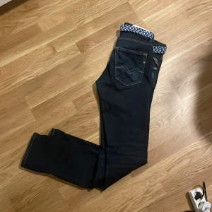 Mörkblå Replay jeans med bälte - Snygga mörkblå jeans från Replay med klassiska kontrastsömmar och femficksdesign. Modellen har raka ben och medföljer ett flätat blåvitt bälte som ger extra stilpoäng. Perfekta för dig som gillar en clean och tidlös look.