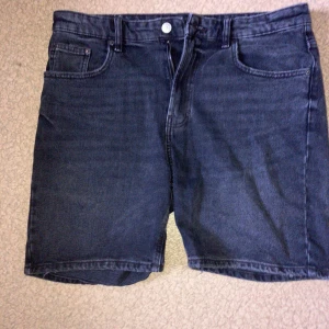 Mörkgrå jeansshorts från Zara - Snygga mörkgrå jeansshorts från Zara med klassisk femficksdesign och raka ben. Shortsen har bälteshällor, knapp och dragkedja framtill samt bakfickor. Perfekta för en chill sommarstil.