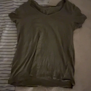 Olivgrön v-ringad t-shirt - En enkel olivgrön t-shirt med v-ringad hals och korta ärmar. T-shirten har en loose passform och är tillverkad i mjukt bomullsmaterial, perfekt för en chill och avslappnad stil.