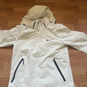 Vit vindjacka med huva från Hzehtk - Snygg vit vindjacka från Hzehtk med svart logga på bröstet. Helt ny Nike jacka i storlek L men skulle säga att den passar mer till M. Ställ gärna frågor om ni undrar något😁!