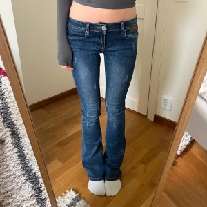 Lågmidjade vida jeans  - Snygga blå jeans från Mywear i bootcut-modell med klassiska fem fickor, slitningar och bruna läder detaljer! Innerbenslängd: 81 cm. Midjeberedd: 32 cm. Benbredd: 21 cm❤️