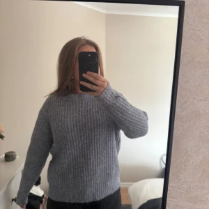 Grå blå  stickad tröja med rund hals - Mysig grå stickad tröja med rund hals och lång ärm. Tröjan har en ribbad struktur och en relaxed passform som är perfekt för kyligare dagar. Enkel att matcha med både jeans och kjol för en avslappnad look. Aldrig använd 
