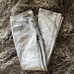 Grå bootcut jeans från Perfect Jeans - Snygga ljusgrå bootcut jeans från Ginatricot med klassiska fem fickor och coola bakfickor med lock och knapp. Jeansen har låg midja och är tillverkade i mjukt denimtyg med lite stretch för extra komfort.
