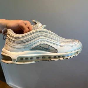 Nike Air Max 97 vita sneakers - Nike Air Max 97 sneakers i vitt med ikoniska vågformade linjer och synlig Air-sula. Skorna har mesh och syntetmaterial, snörning och rund tå. Skorna är använda hyfsat mycket men fortfarande fungerande. Storlek 44,5. Hör gärna av er om ni har några frågor!!