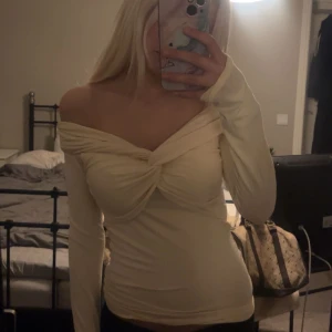 Offshoulder topp från Gina Tricot - Säljer en ljusbeige offshoulder topp från Gina Tricot i storlek S. Toppen har lång ärm, twistad detalj framtill och sitter tight. Perfekt för dig som gillar en stilren och trendig look. Materialet är mjukt och stretchigt för en bekväm passform.