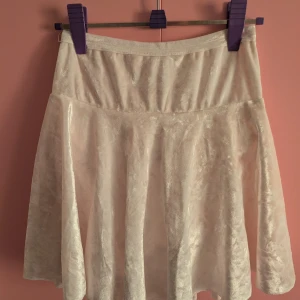 Vit konståkning sammetskjol med inbyggda shorts - Supersöt vit kortkjol i sammetsmaterial med inbyggda shorts under. Kjolen har en lätt glansig yta och är perfekt för dig som vill ha både stil och komfort. Den har en enkel midja och ett flowy fall som ger en snygg siluett. Stor i storlek. Ca storlek Large 