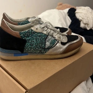 Philippe Model sneakers med leopardmönster - Unika sneakers från Philippe Model med blått leopardmönster, detaljer i silver, svart och brunt. Skorna har snörning, platt sula och är tillverkade i en mix av skinn och mocka. Perfekta för dig som vill sticka ut med en cool och färgstark stil.