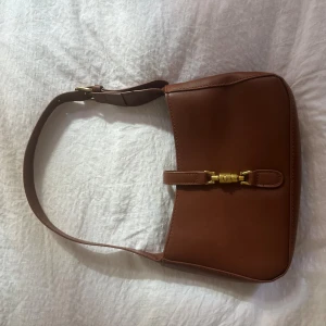 Brun axelväska med gulddetalj - Får plats med telefon, korthållare, läppenna, läppglans och 30 ml parfymflaska.