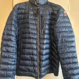 Mörkblå dunjacka Parajumpers M - Snygg mörkblå dunjacka från Parajumpers, modell Sheen. Jackan har quiltad design, dragkedja framtill och flera fickor. Klassisk PJS-patch på ärmen och röd insida som ger en cool kontrast. Perfekt för kyliga dagar och riktigt stilren look. Den är lite trasig vid fickan på framsidan (syns på bild 4)