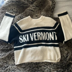 Randig stickad tröja från H&M - Säljer en stickad tröja från H&M med texten 'SKI VERMONT' framtill. Tröjan är svart och vit med breda ränder och ribbade muddar. Den har en klassisk rund halsringning och långärmade ärmar. Perfekt för kalla dagar och snygg till jeans.
