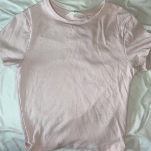 Ljusrosa croppad t-shirt från Gina Tricot - Säljer en ljusrosa smått croppad t-shirt från Gina Tricot, basically basics. T-shirten har rund hals och korta ärmar, tillverkad i mjuk bomull. Perfekt för dig som gillar enkla och stilrena plagg med en fräsch vibe.