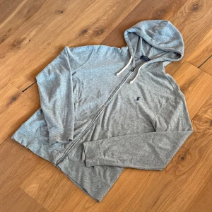Polo Ralph Lauren Hoodie - Grå hoodie från Polo Ralph Lauren med dragkedja framtill, vit snörning i huvan och klassisk broderad logga på bröstet. 