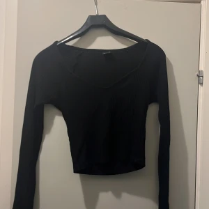 Svart croppad långärmad topp - Säljer en svart croppad topp med lång ärm och v-ringad hals. Toppen har en tight passform och är tillverkad i ett stretchigt material som sitter snyggt på kroppen. Perfekt att matcha med höga jeans eller kjol.