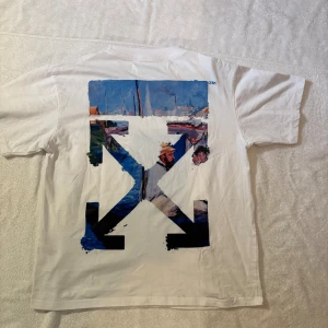 Vit Off-White t-shirt med konsttryck - Vit t-shirt från Off-White med namnet på bröstet och stort färgstarkt konstinspirerat tryck på ryggen. Skön passform och tillverkad i mjuk bomull. Väldigt lätt och sitter fantastiskt på mig som är 179 65kg och brukar bära S/M, skulle säga att det är en M. Kolla profilen för mer