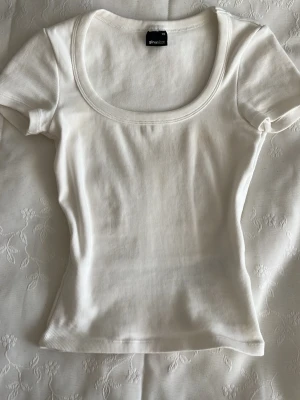 Vit ribbad topp från Gina Tricot - Säljer en vit ribbad topp från Gina Tricot i storlek XS. Toppen har rundad urringning, korta ärmar och sitter tight.