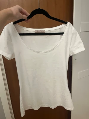 Vit t-shirt med rund hals från Anna Field - En basic vit t-shirt från Anna Field med rund, djup urringning och korta ärmar. Modellen är figurnära och tillverkad i mjuk bomull som känns skön mot huden. Perfekt att styla med jeans eller kjol. Endast använd en gång🩷🩷
