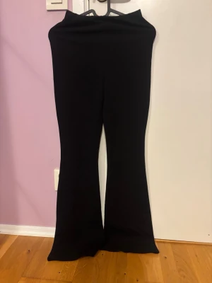 Svarta bootcut byxor - Säljer ett par svarta bootcut byxor med hög midja. Byxorna har en mjuk och stretchig känsla, perfekta för dig som gillar en bekväm men ändå snygg look. Passformen är tight upptill och släpper ut vid bensluten för en klassisk siluett.