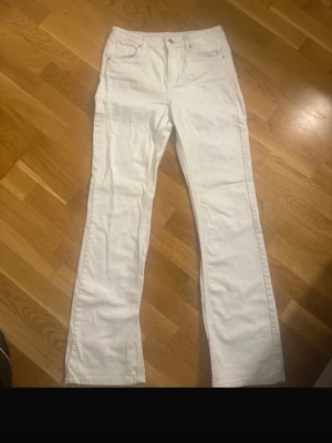 Vita bootcut jeansbyxor - Säljer ett par vita jeansbyxor med klassisk femficksdesign och bootcut passform. Byxorna har hög midja och är tillverkade i ett mjukt bomullsmaterial. Perfekta för dig som vill ha en clean och fräsch look.