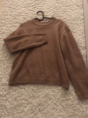 Beige stickad tröja från 157 - Mysig ”brun-ish” stickad tröja från 157 med rund halsringning och långa ärmar. Perfekt för lager på lager och chill dagar. Enkel och stilren design som passar till det mesta.