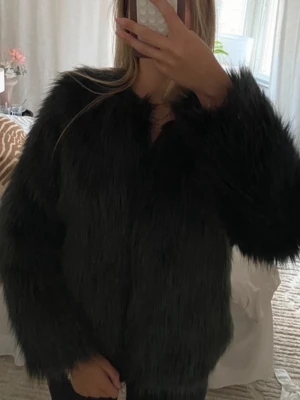 Mörkgrön pälsjacka  -  fluffig fuskpäls och helsvart innerfoder. Jackan har en rak passform och långa ärmar, perfekt för dig som vill ha en statement piece till garderoben.