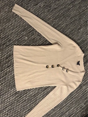 Beige ribbad topp med knappar - • Ribbad topp från Lindex i storlek S • Använd max 2-3 gånger (ser oanvänd ut, se bilderna ovan) • Nypris: 399 kr  • Super bra kvalitet då tyget är tjockt och ser ”dyrt” ut  Pris kan diskuteras vid snabbt köp 😊🤍