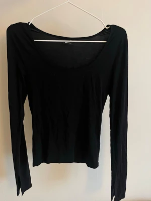 Svart långärmad topp  - En enkel svart långärmad topp från Gina Tricot med rundad, djup urringning. Modellen är tight med slit längst ner på ärmarna. 