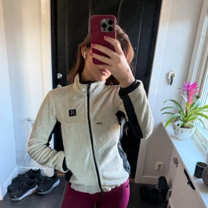 Fleecejacka från Haglöfs - Säljer en vit och svart fleecejacka från Haglöfs med Windstopper-funktion. Jackan har hel dragkedja, hög krage och långa ärmar. Perfekt för kyliga dagar och outdoor-aktiviteter. Mysig och mjuk med svarta paneler på sidorna och ärmarna💛🧡